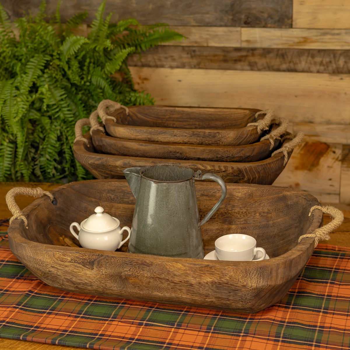 Nested wooden trays behind a larger tray arranged with a pitcher, teapot, and cup.