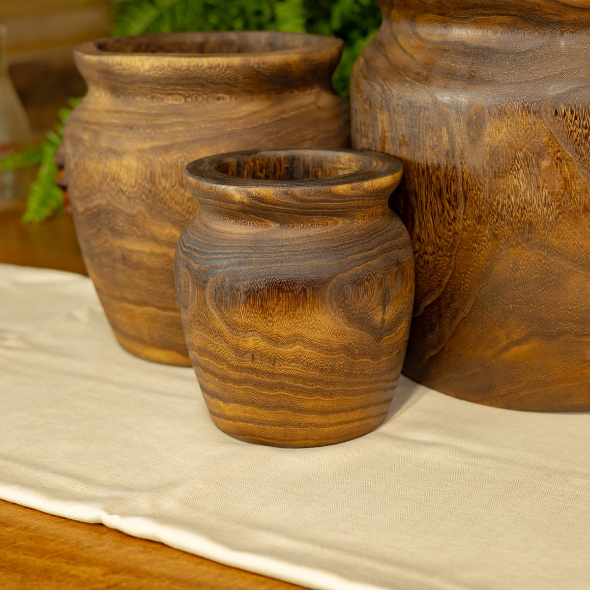 Small round planter in front of two larger matching planters, showing its dark swirling grain.
