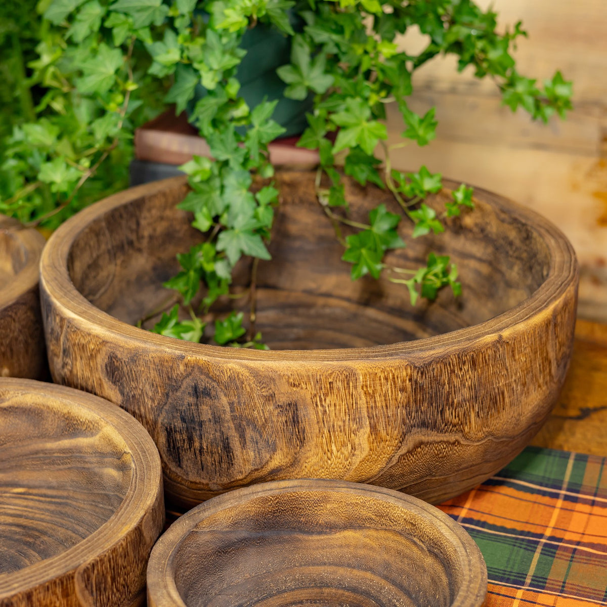 Close-up of the large wooden bowl's rounded rim and textured grain, with smaller bowls partly visible.