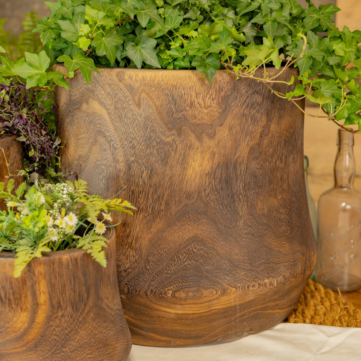 A large wooden bowl filled with trailing green leaves, with part of a smaller bowl visible beside it.