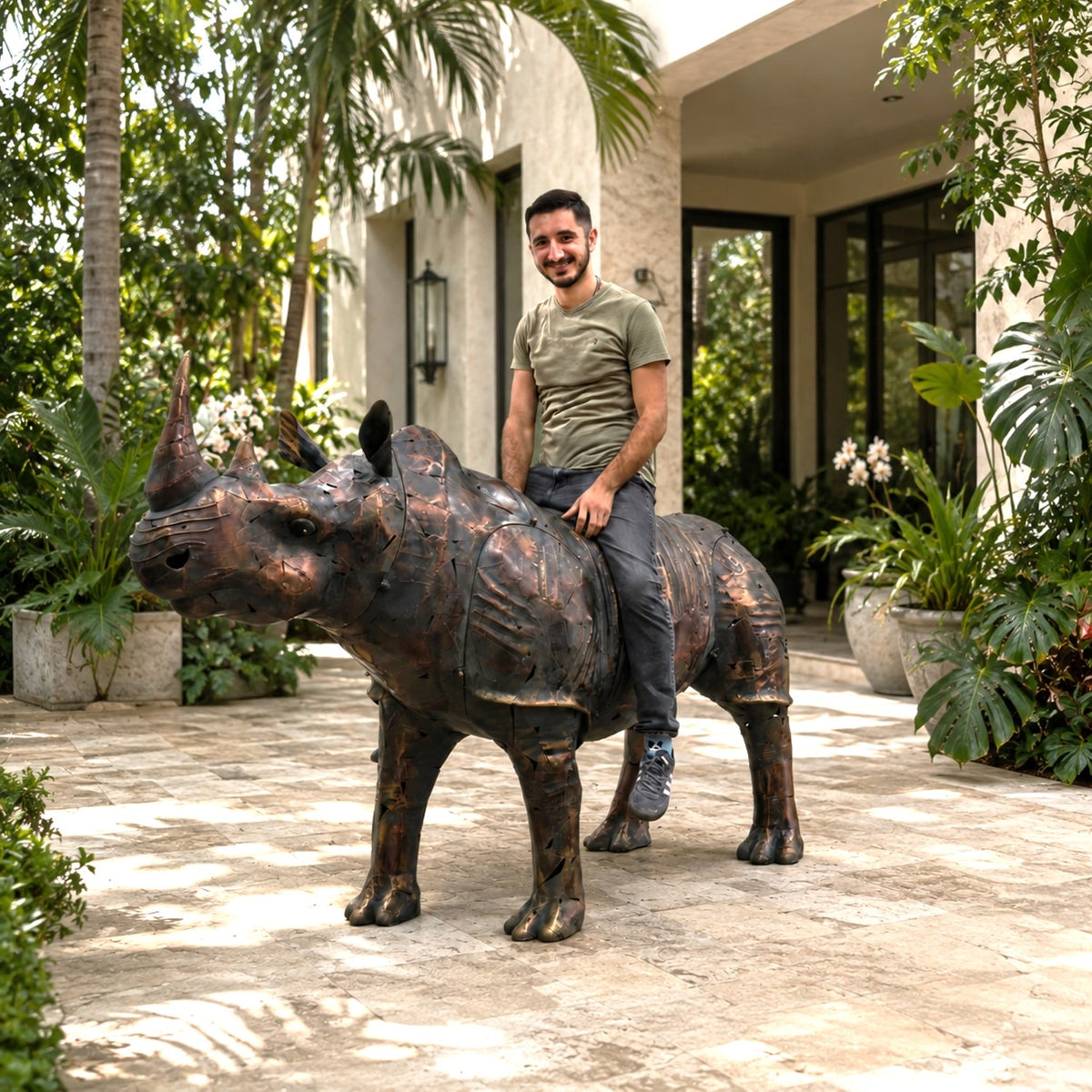 Person seated on a large iron rhinoceros statue in a landscaped courtyard