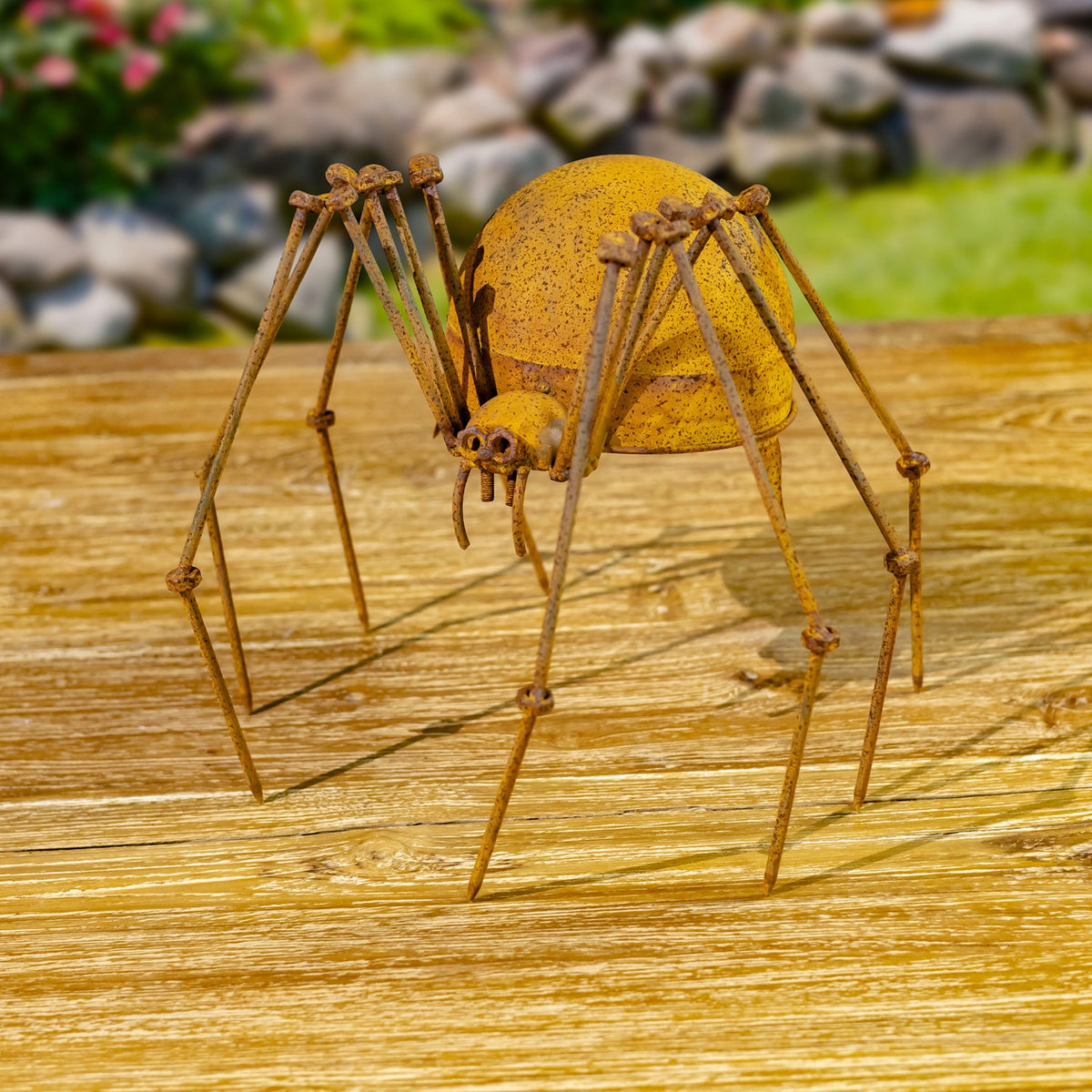 Rust-finish iron spider figurine angled on a wooden surface outdoors