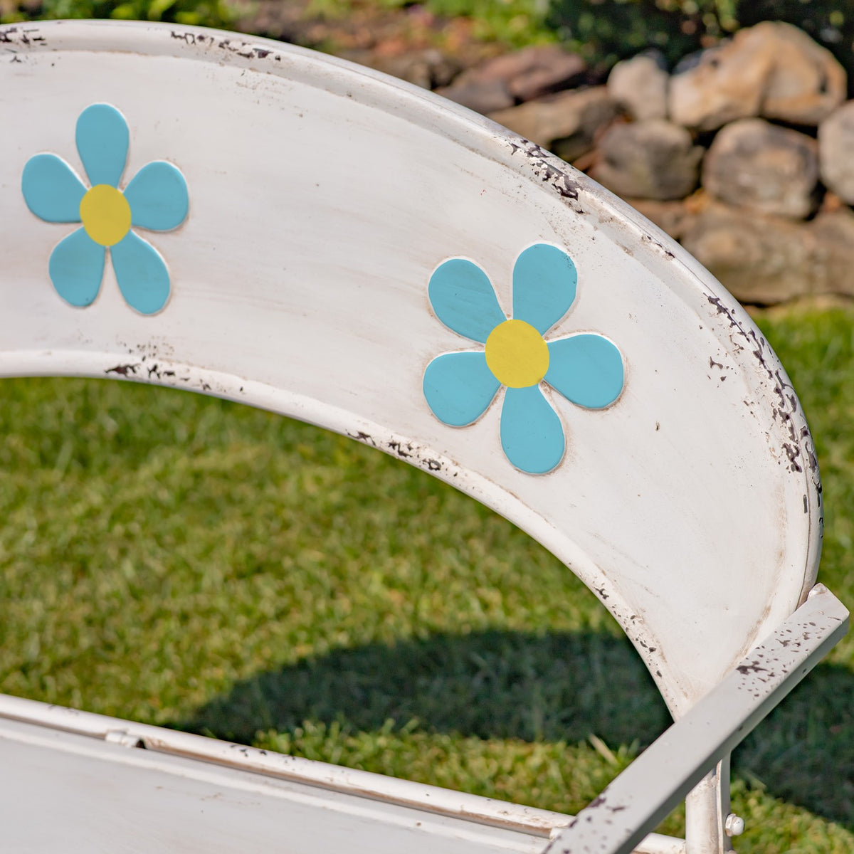 Two blue flowers with yellow centers decorate the curved, weathered white bench backrest.