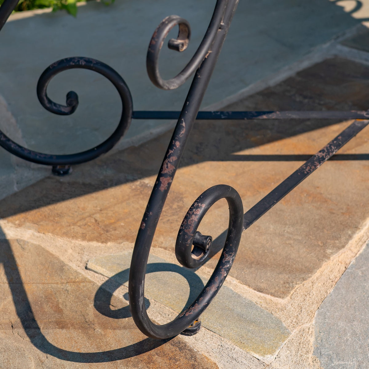 Close-up of the table’s curved black iron legs and crossbars on a stone patio.