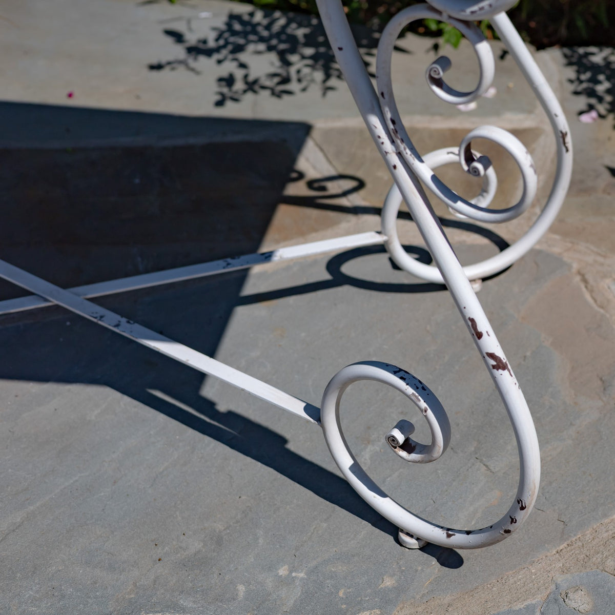 Close-up of a white curled iron table leg with chipped paint on a stone patio.