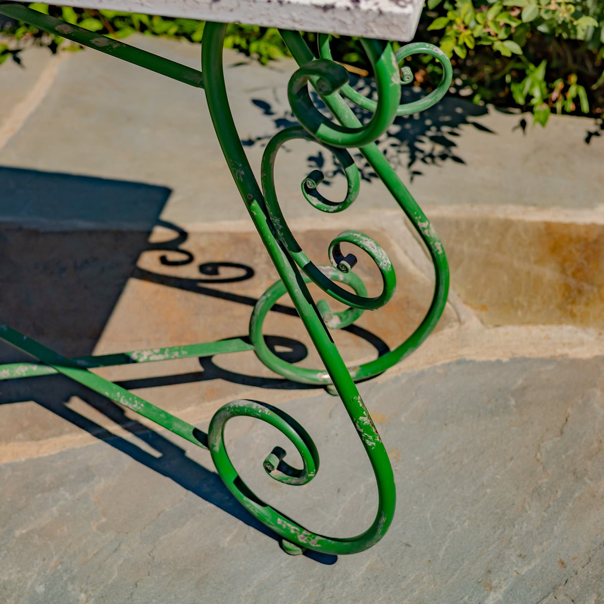 Close-up of green curled iron table legs beneath a distressed white tabletop.