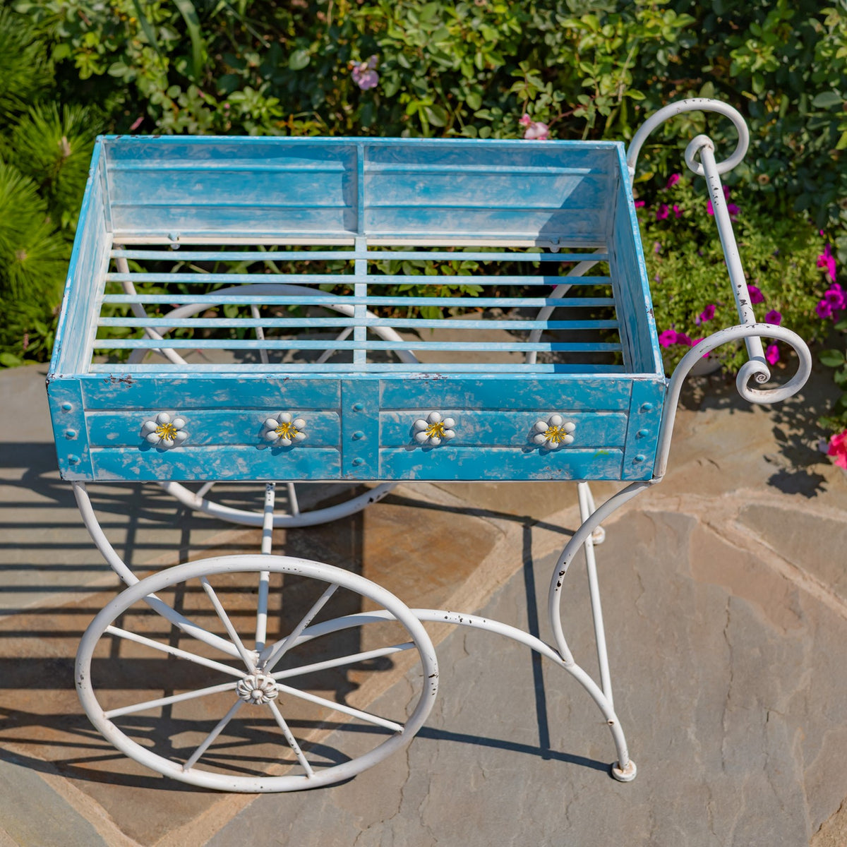 Top-down view into the empty blue cart, showing its slatted base and curled handle beside the flower bed.