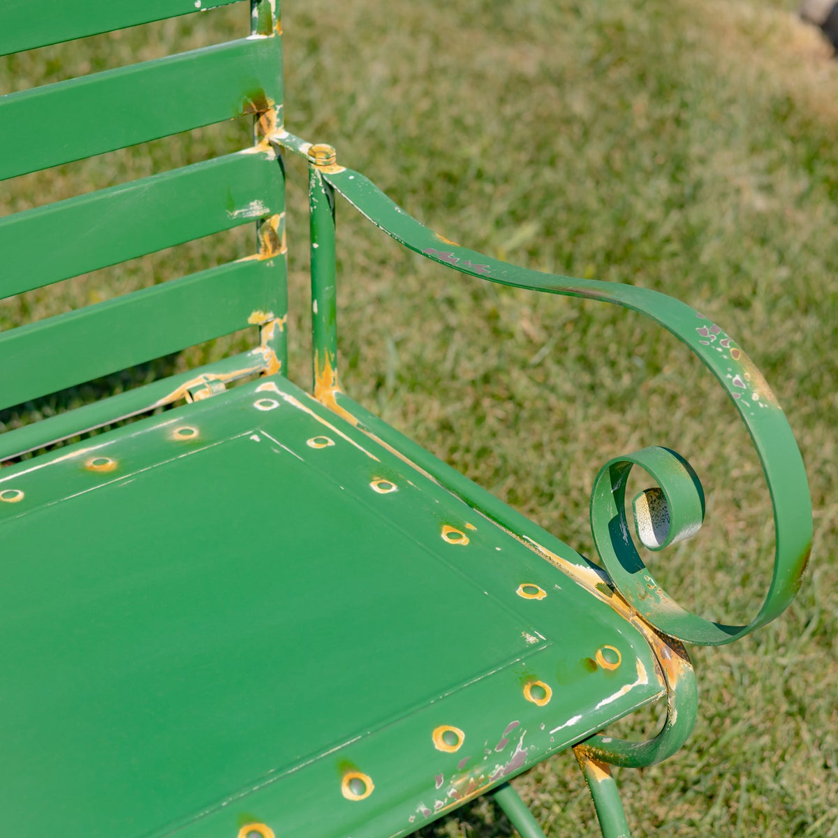 Close-up of the curled metal arm beside the seat, with gold-toned accents and distressed paint.