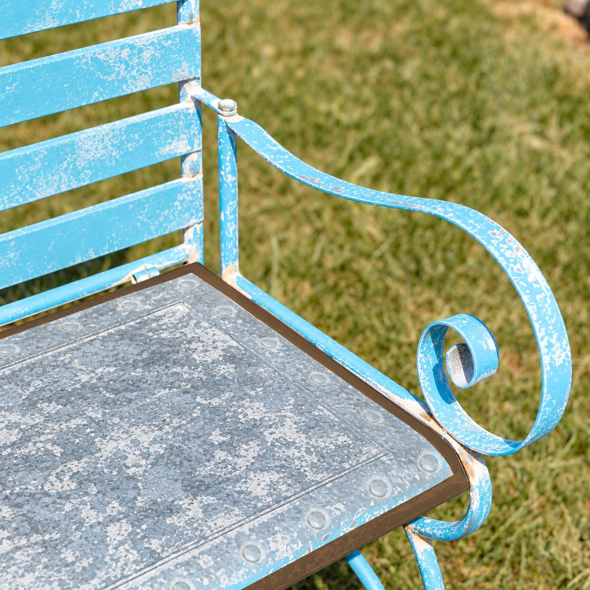 Angled view of the blue bench’s curved armrest beside its patterned metal seat and slatted back.