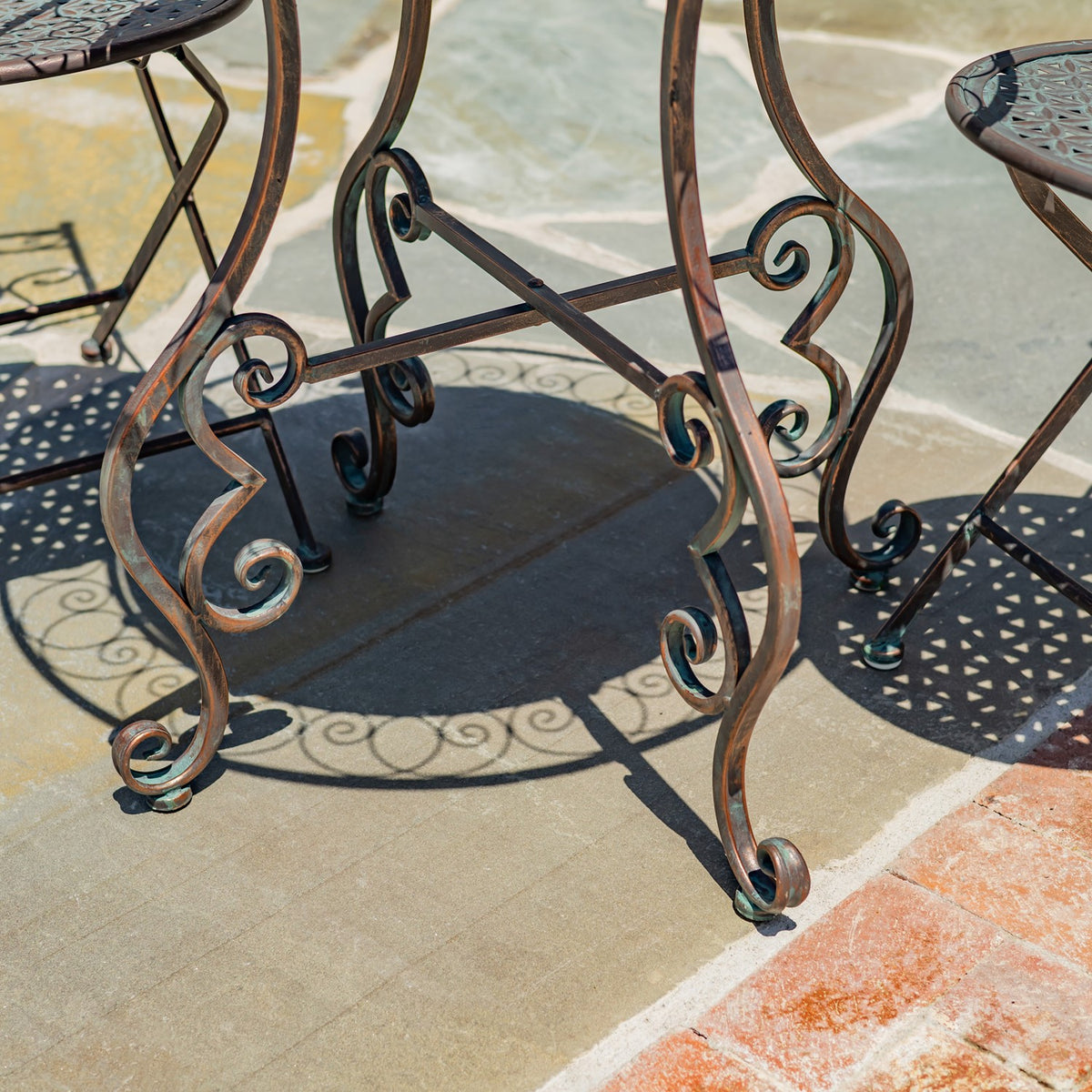 Close-up of the table’s curled metal legs and cross braces casting patterned shadows on the patio.