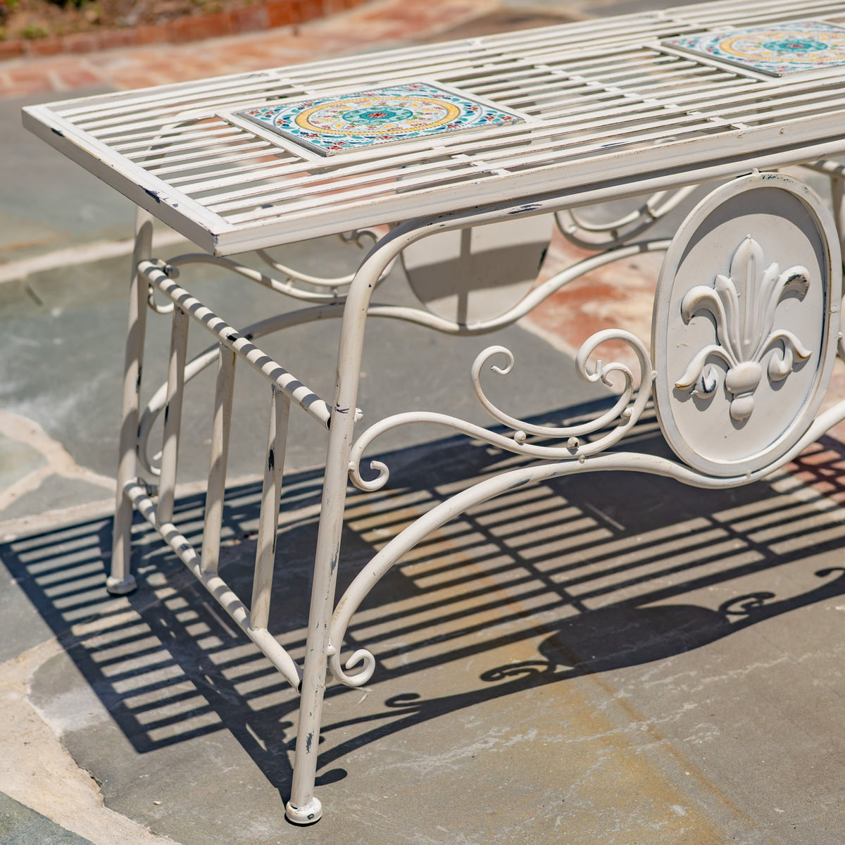 Close view of the table's mosaic inset, curved metal supports, and raised central ornament.