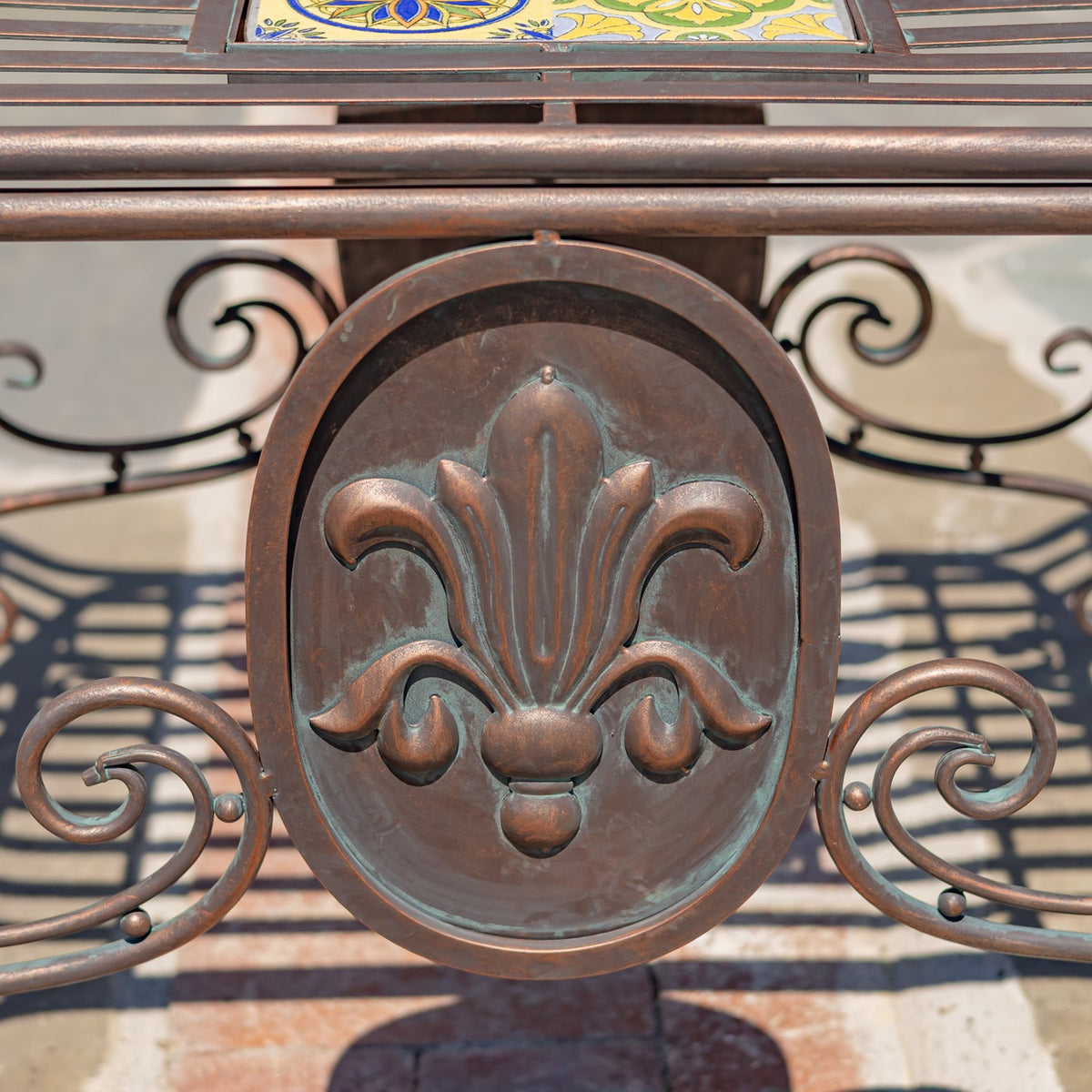 Close-up of a raised fleur-de-lis medallion and curled metalwork beneath the mosaic seat.