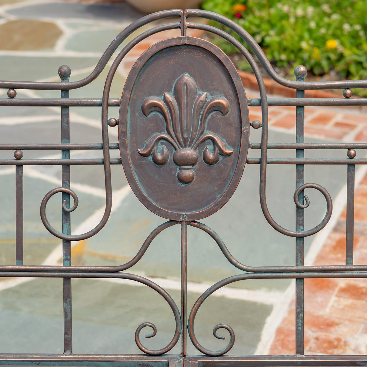 Close-up of an embossed fleur-de-lis medallion framed by curved metalwork on the bench back.