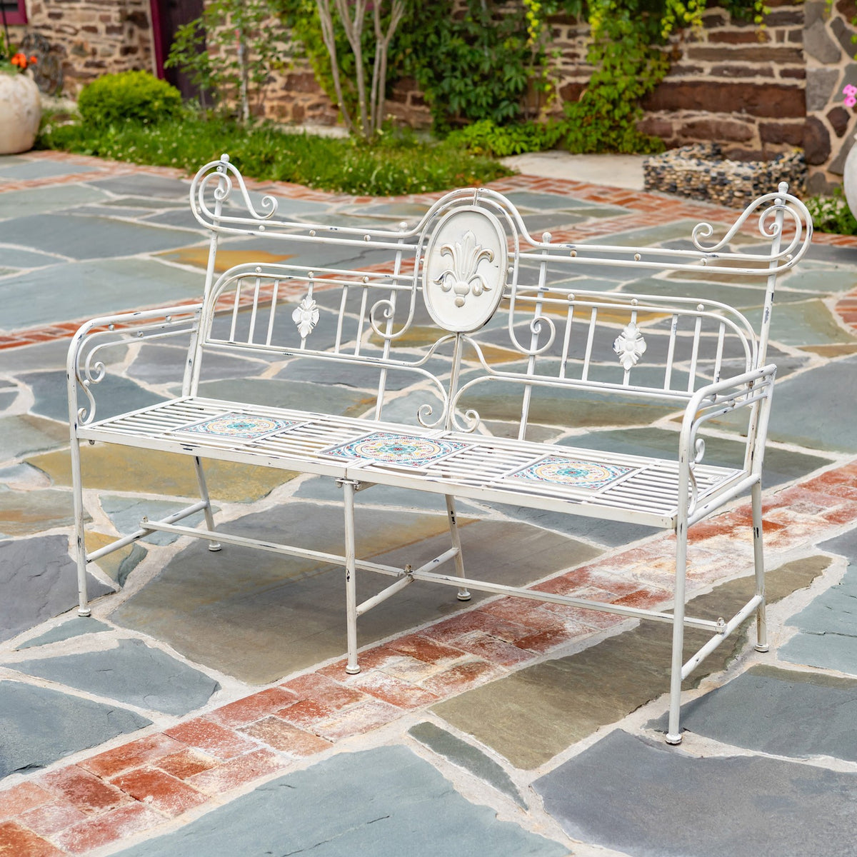 Three-quarter view of the ornate metal bench with patterned tiles across its slatted seat