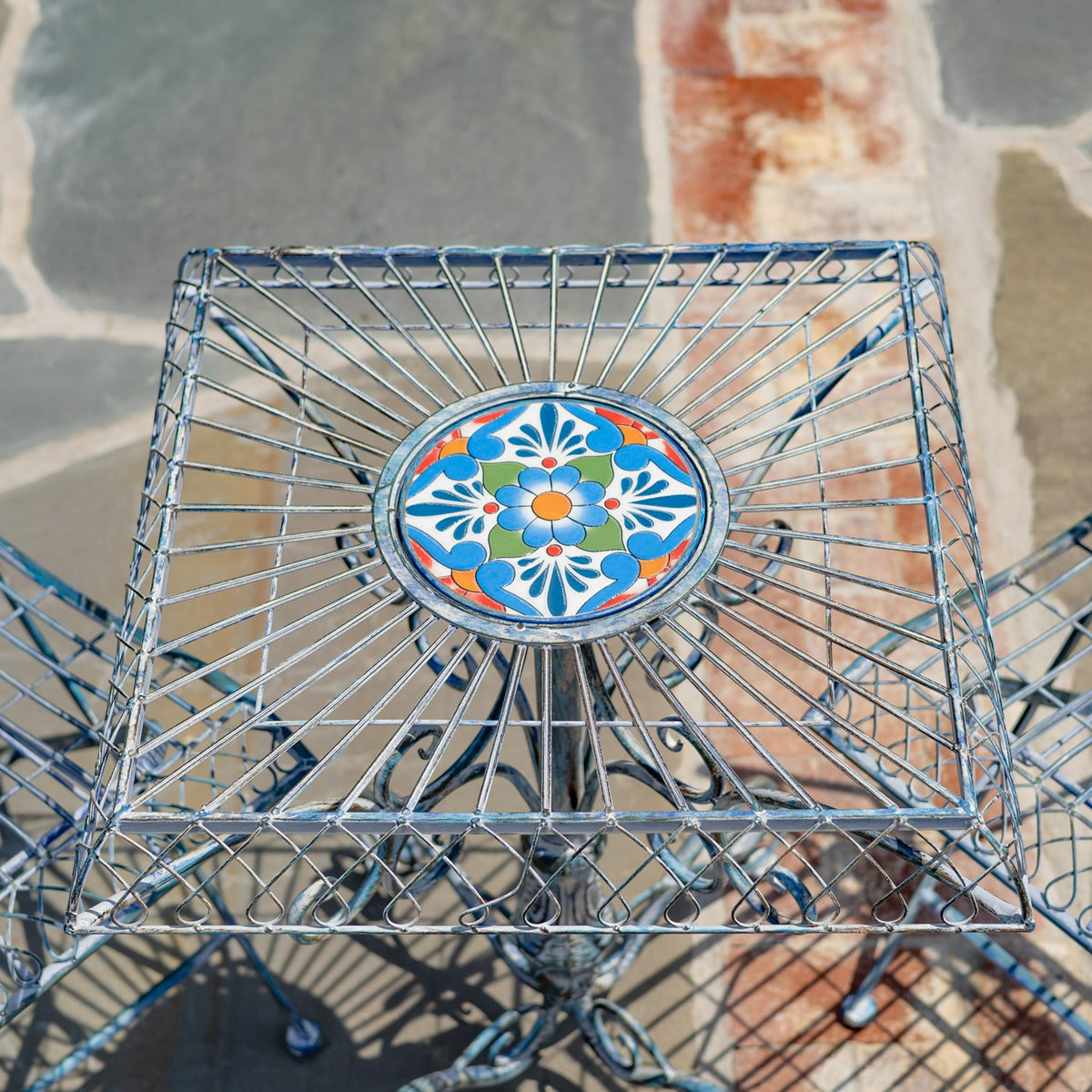 Overhead close-up of the table's radial metalwork surrounding a bright floral mosaic tile.