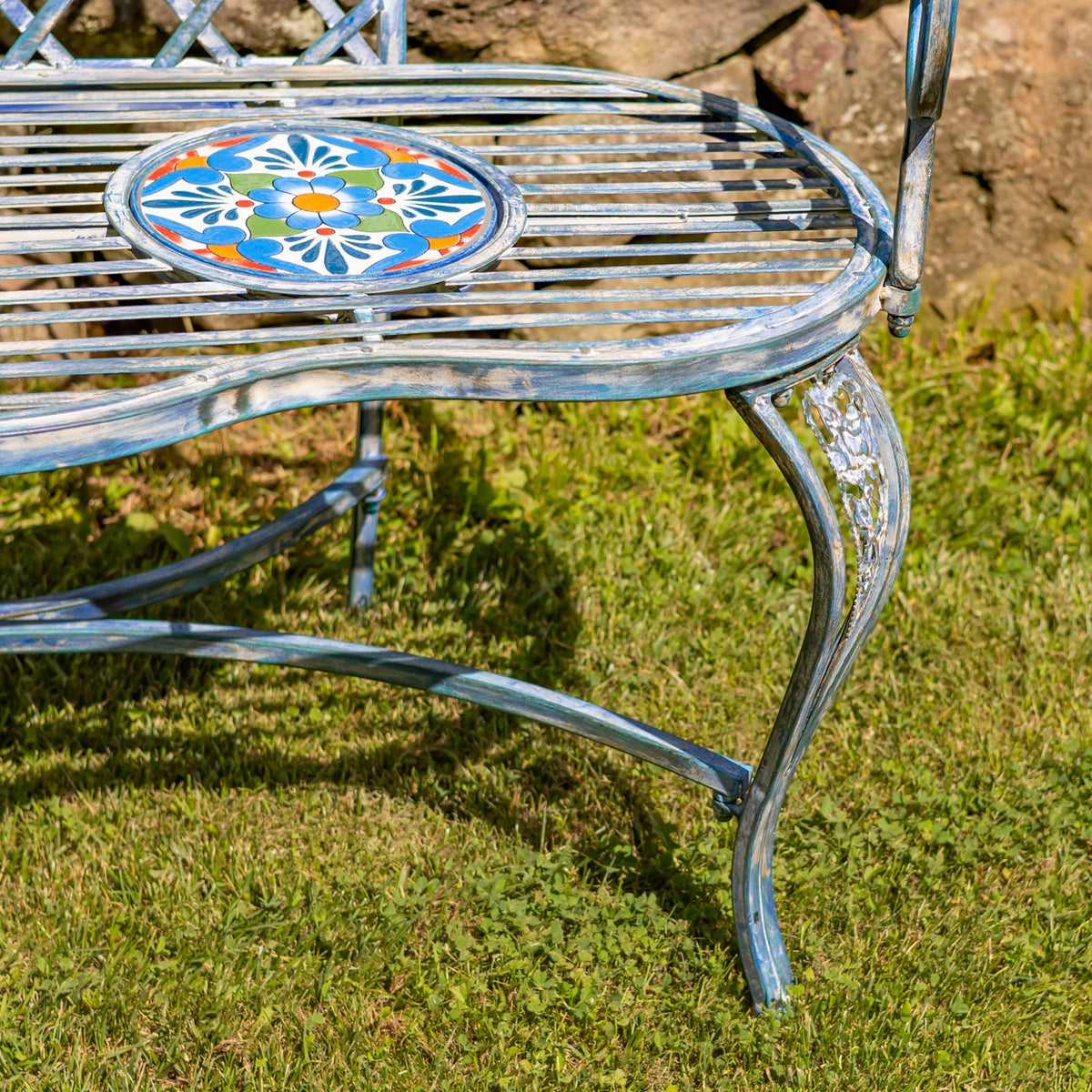 Close-up of a mosaic seat medallion, curved metal leg, and slatted bench seat.