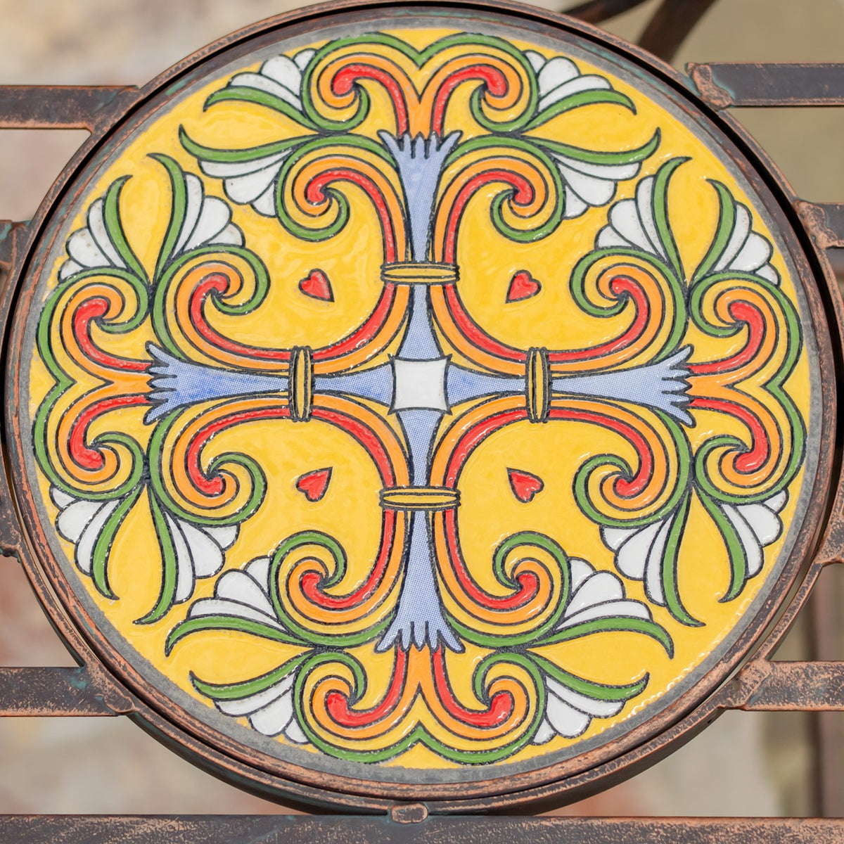 Close-up of a round mosaic tile with a symmetrical yellow, orange, blue, and white floral pattern.