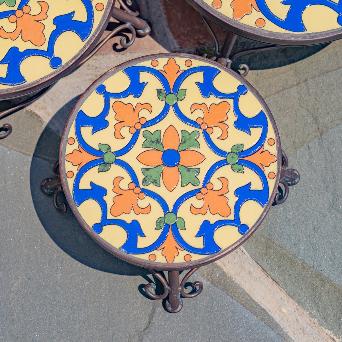 Overhead close-up of a round tabletop with a blue, cream, orange, and green mosaic pattern.