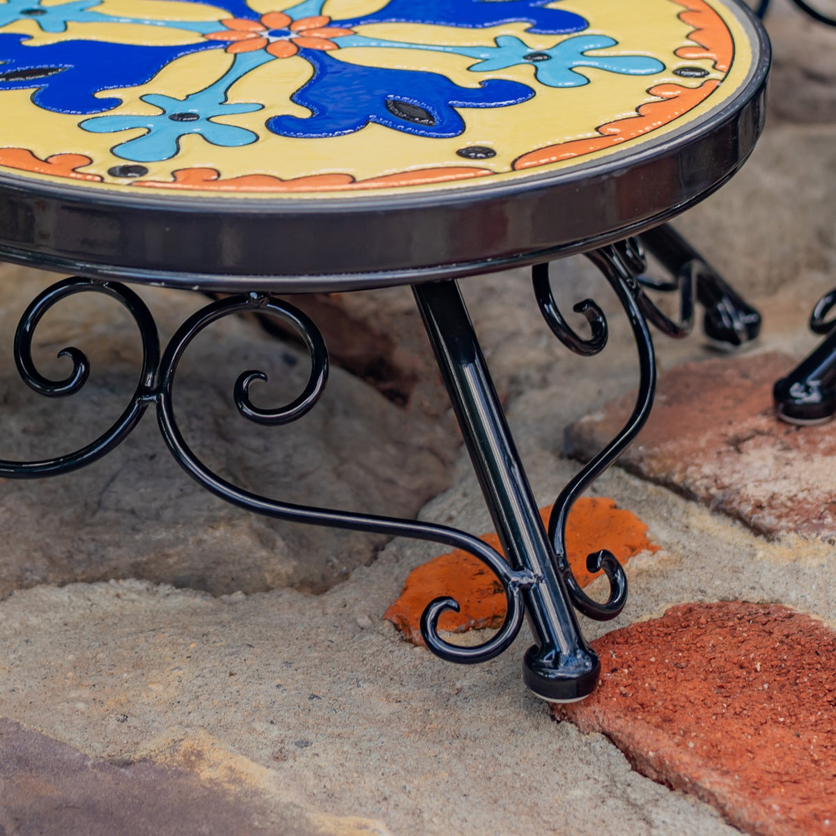 Close view of a curled black metal leg beneath the mosaic tabletop.
