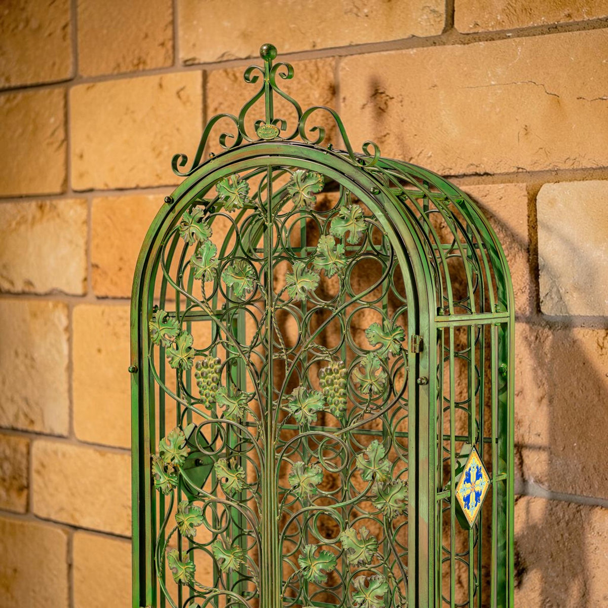 Close-up of the rack's arched iron scrollwork, grapevine decoration, and colorful side tile.