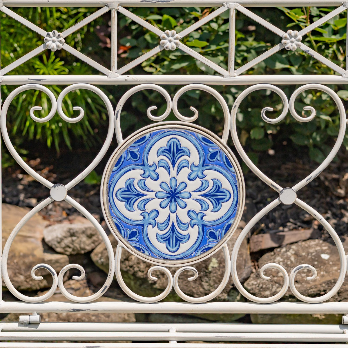 Blue floral mosaic medallion framed by curled antique-white metalwork on the bench back.