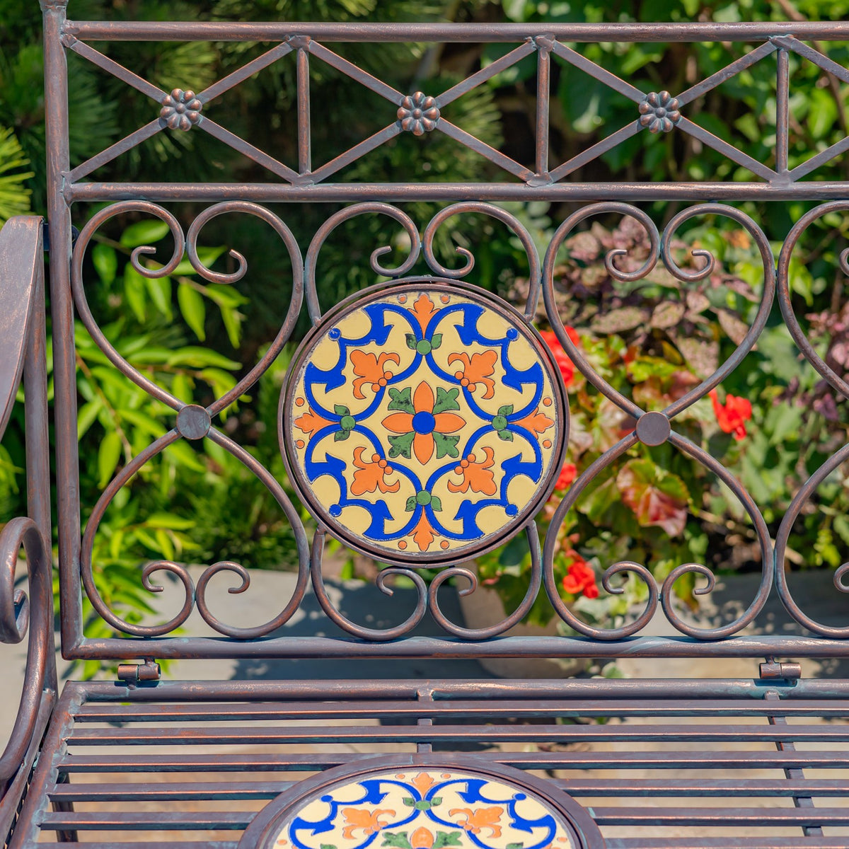 Close-up of a round floral mosaic panel framed by curled metalwork above the slatted seat.