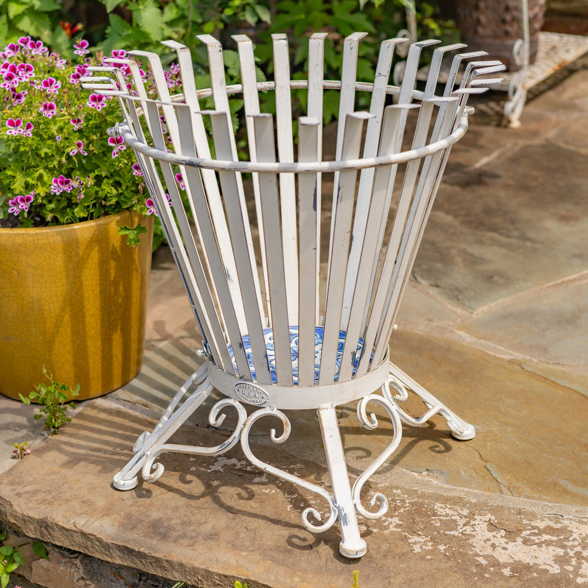 An empty white iron basket stand shows its open slatted sides and curled metal feet.