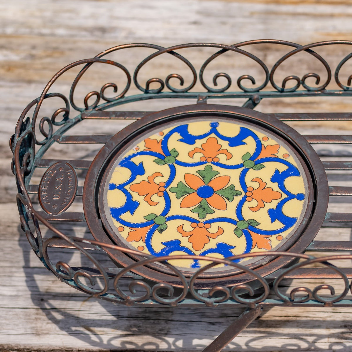 Close-up of a colorful floral mosaic tile set within the stand’s bronze scrollwork.