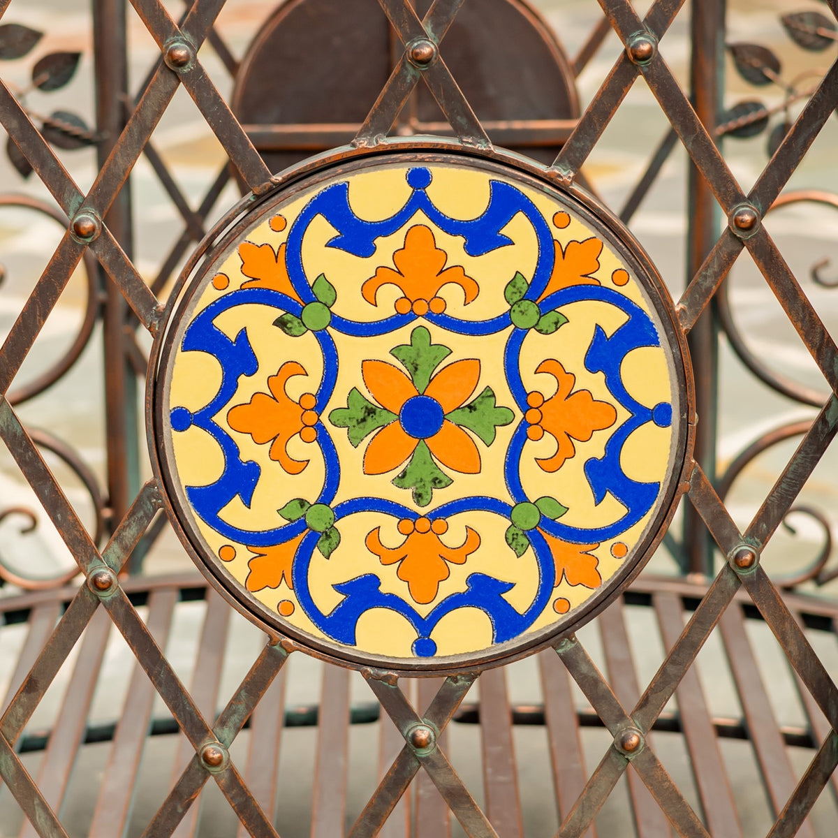 Round ceramic-looking panel with a vivid blue, yellow, orange and green floral pattern in a metal frame.