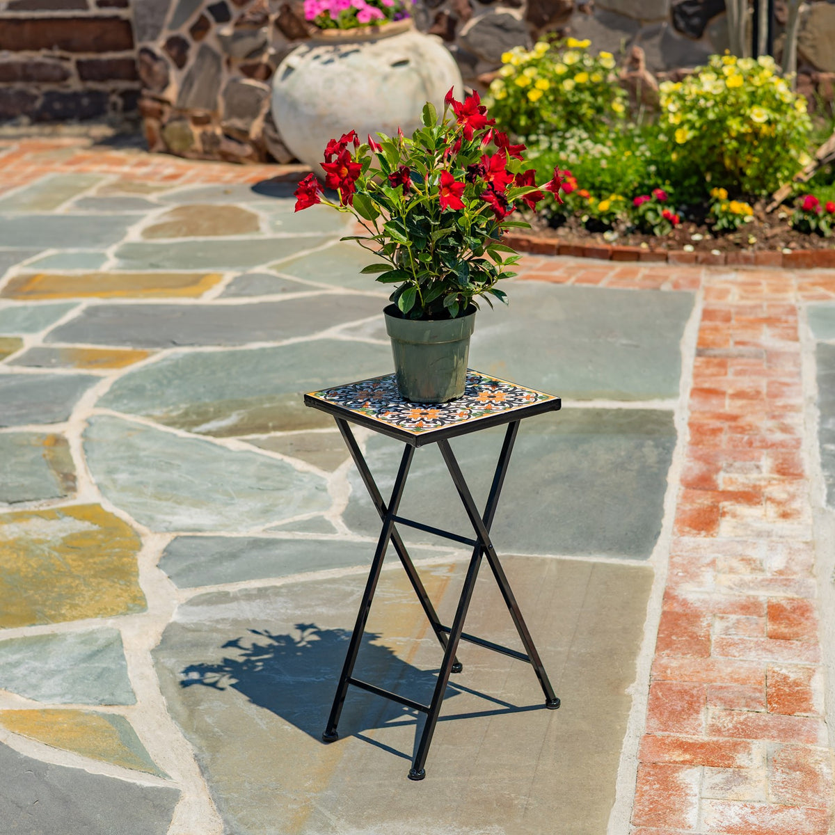 The folding stand supports a potted plant, shown among stone paving and garden beds.