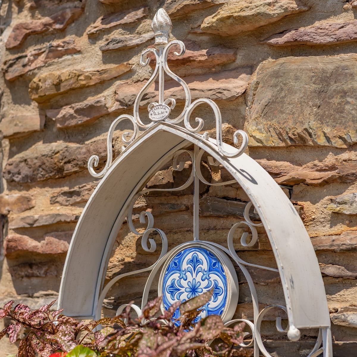Close-up of the planter’s curled metal crest and blue patterned tile against stone.