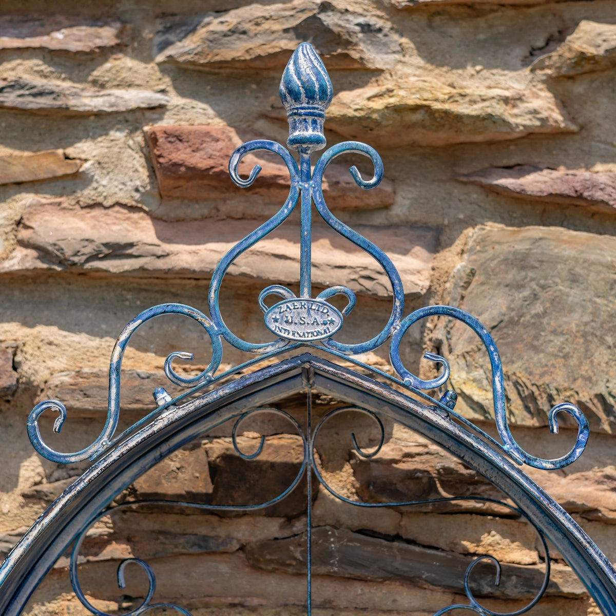Close-up of the planter’s blue iron crest and curled scrollwork against stone.