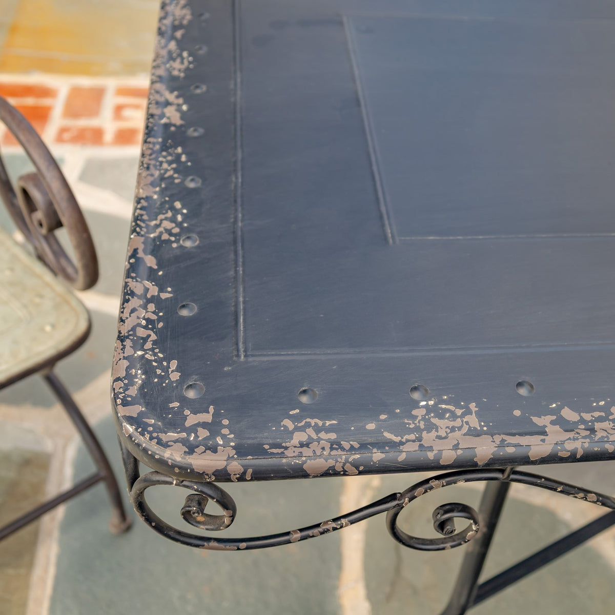 Close-up of a dark metal tabletop with a worn, distressed edge and scrollwork beneath.