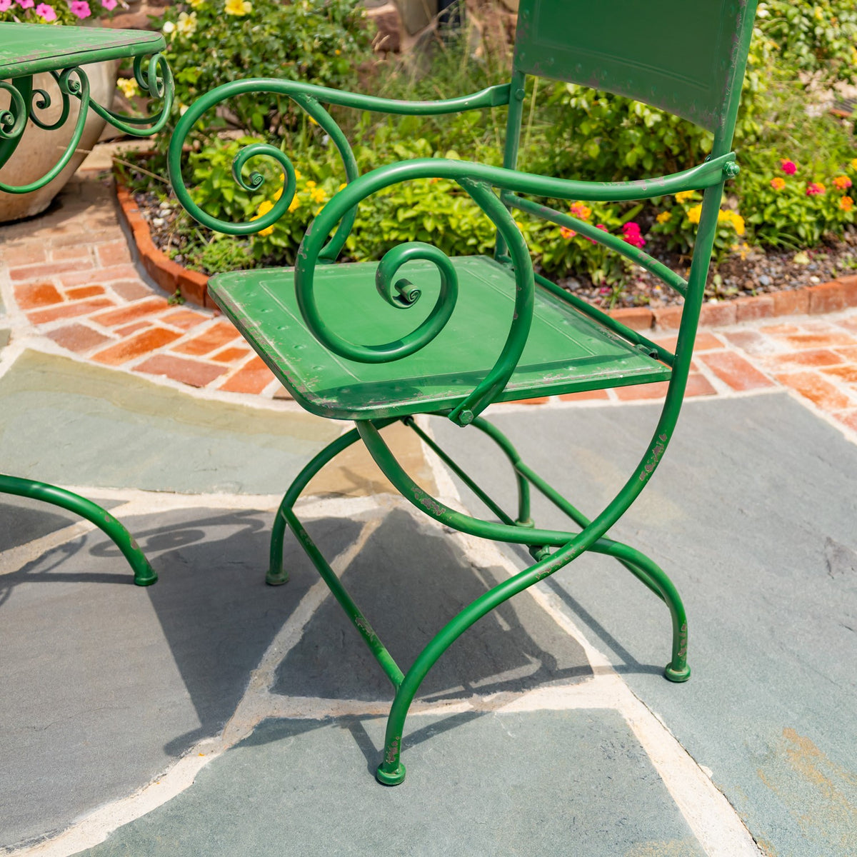 Angled close-up of a green metal chair highlighting its curled armrest, flat seat and curved legs.