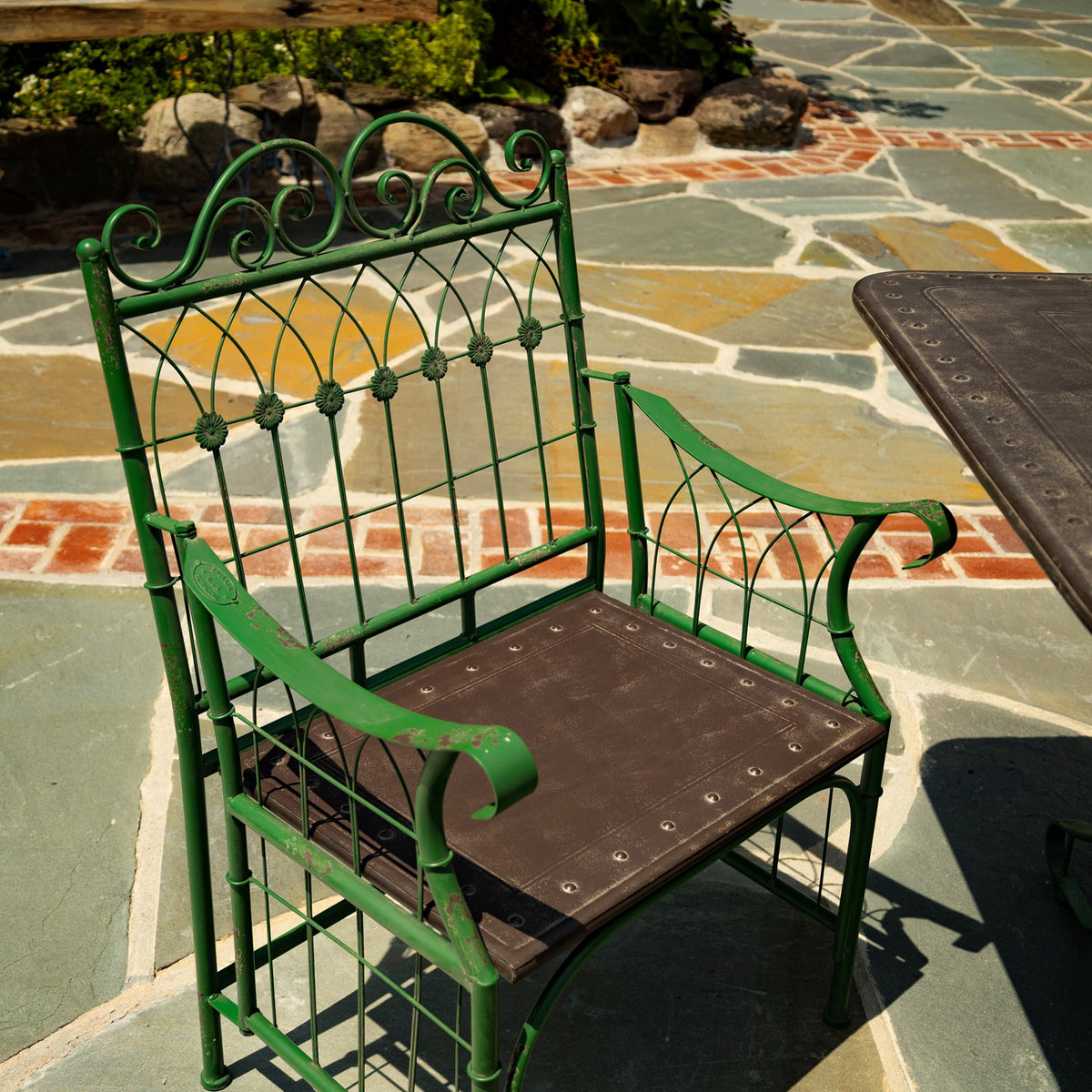 Green metal chair with curled arms and decorative back beside the edge of the tabletop.