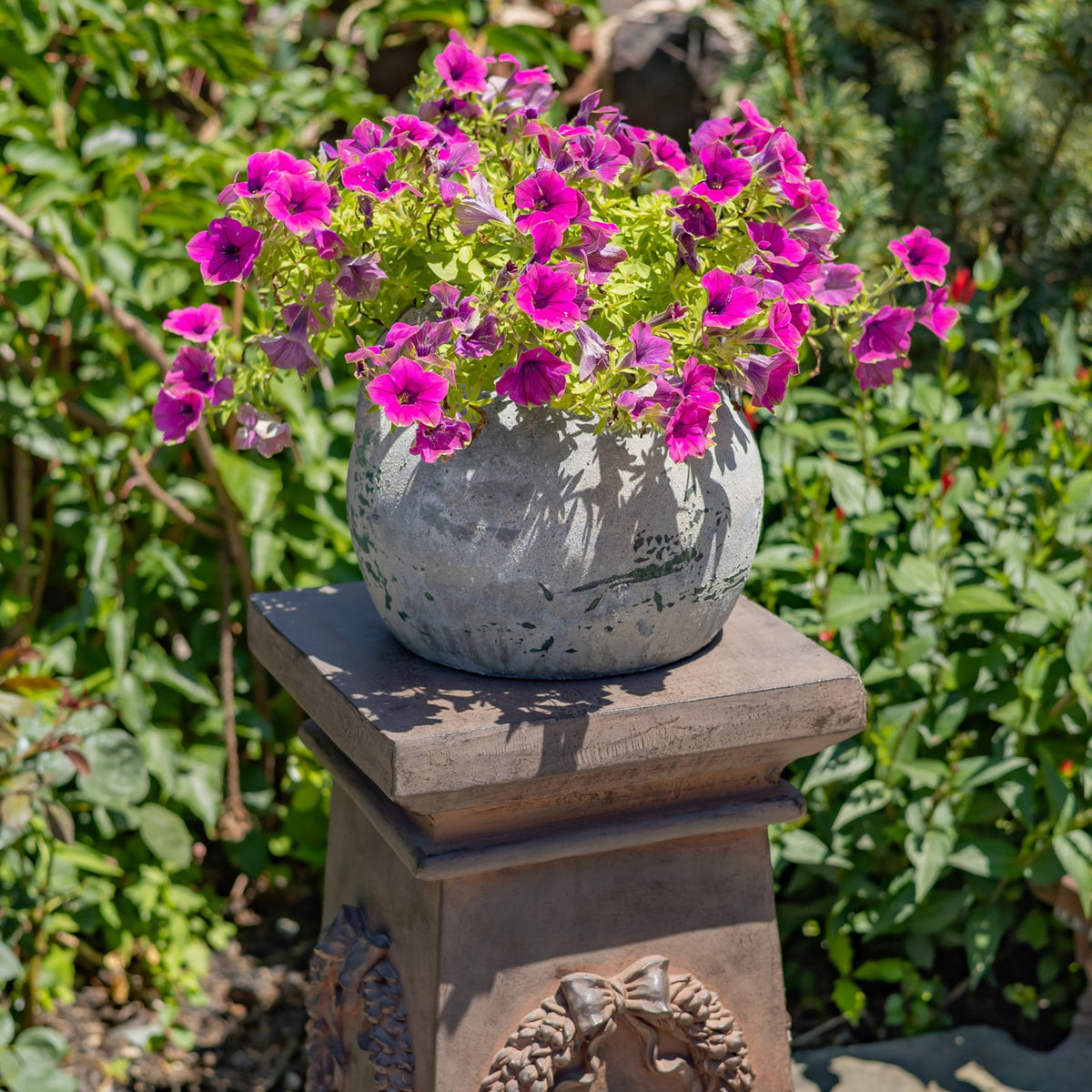 A gray planter filled with bright pink flowers sits atop a square decorative column.