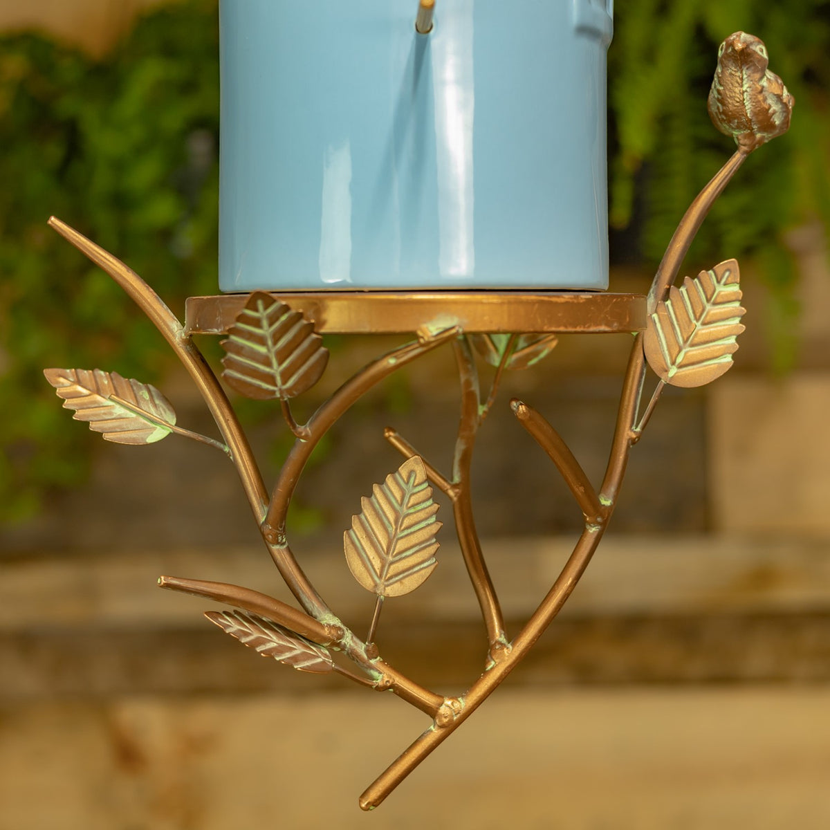 Close-up of the bronze-toned branch frame with leaf ornaments beneath the blue birdhouse.