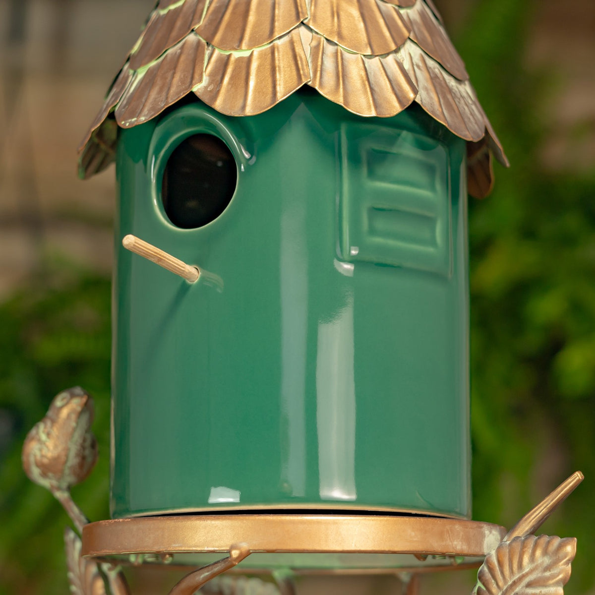 Close view of the birdhouse's opposite side, showing a rectangular panel, round opening, perch, and metal leaf accents.