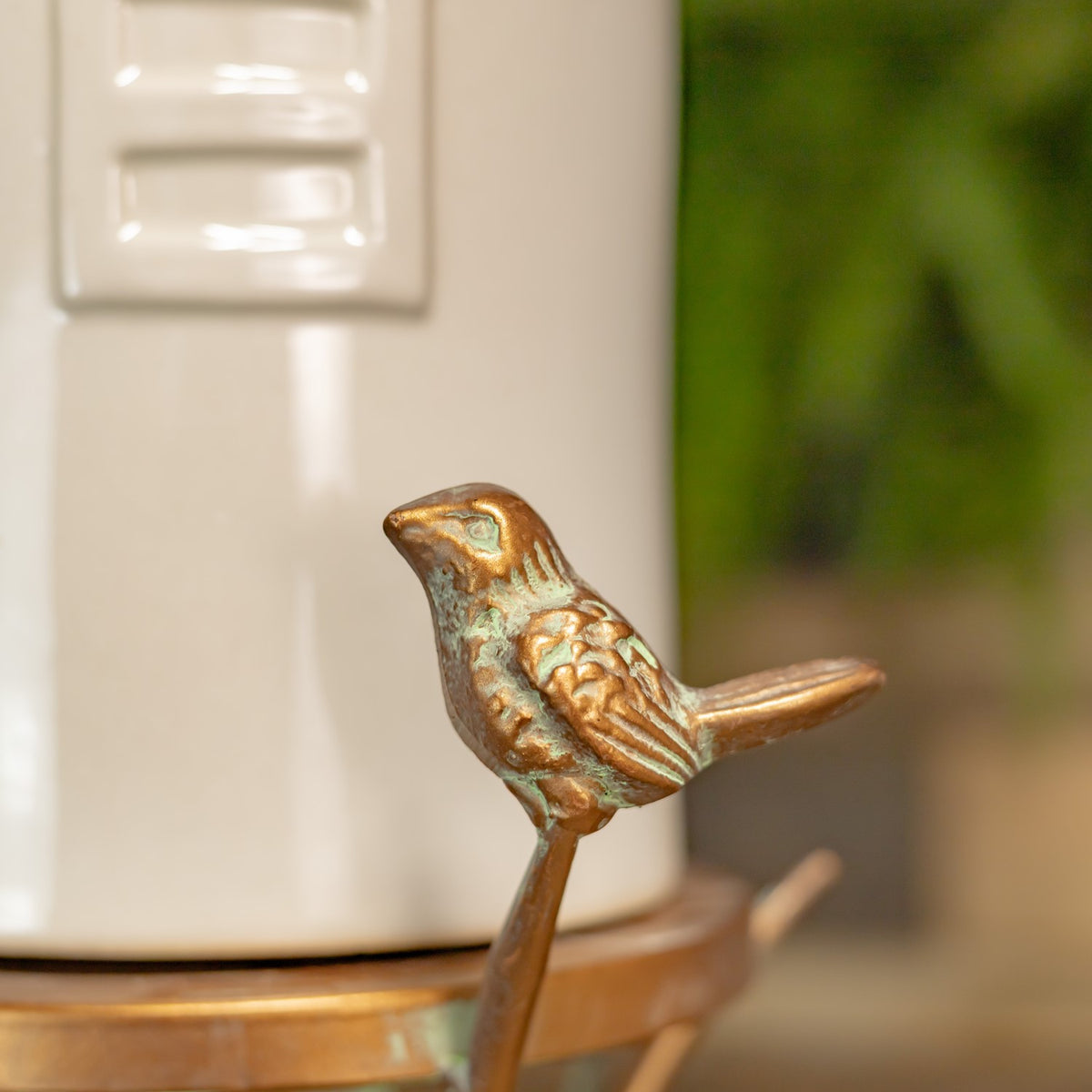 Small copper-tone bird ornament perched on a branch beside the birdhouse body.