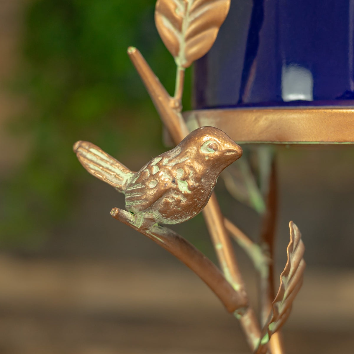 Small sculpted bird ornament perched among copper-colored branches and leaves.