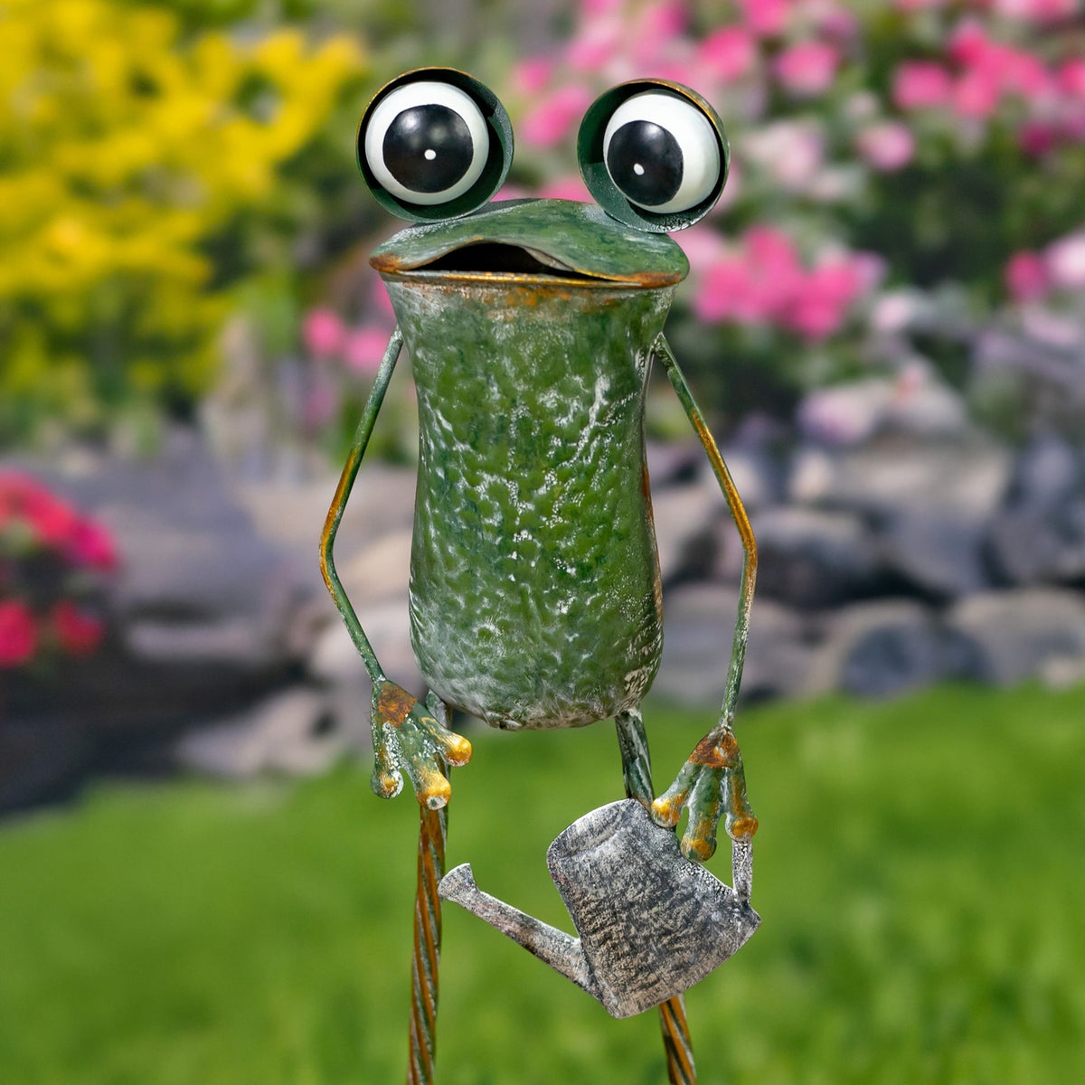 A green metal frog with large round eyes holds a small textured watering can.
