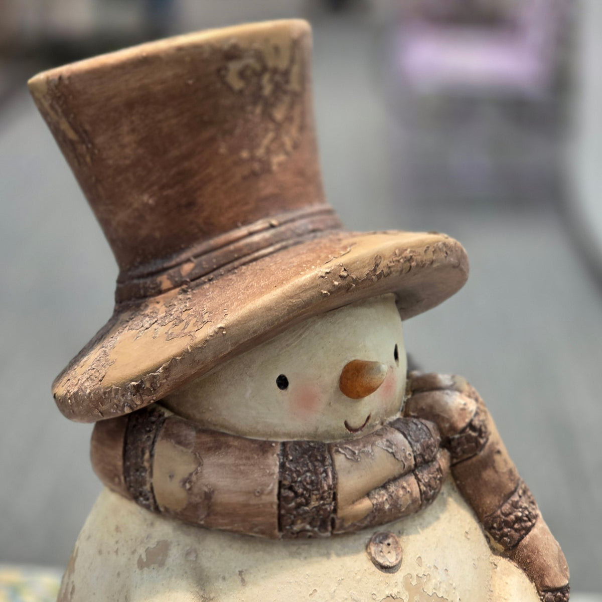 Close view of the snowman’s worn brown hat, segmented scarf, painted face, and upper body.
