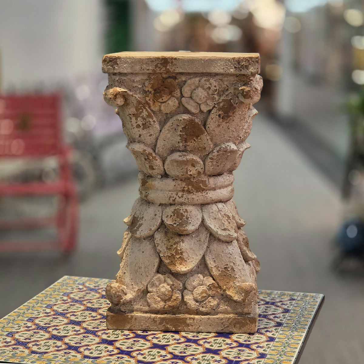 Full front view of the distressed carved pedestal stand on a patterned table