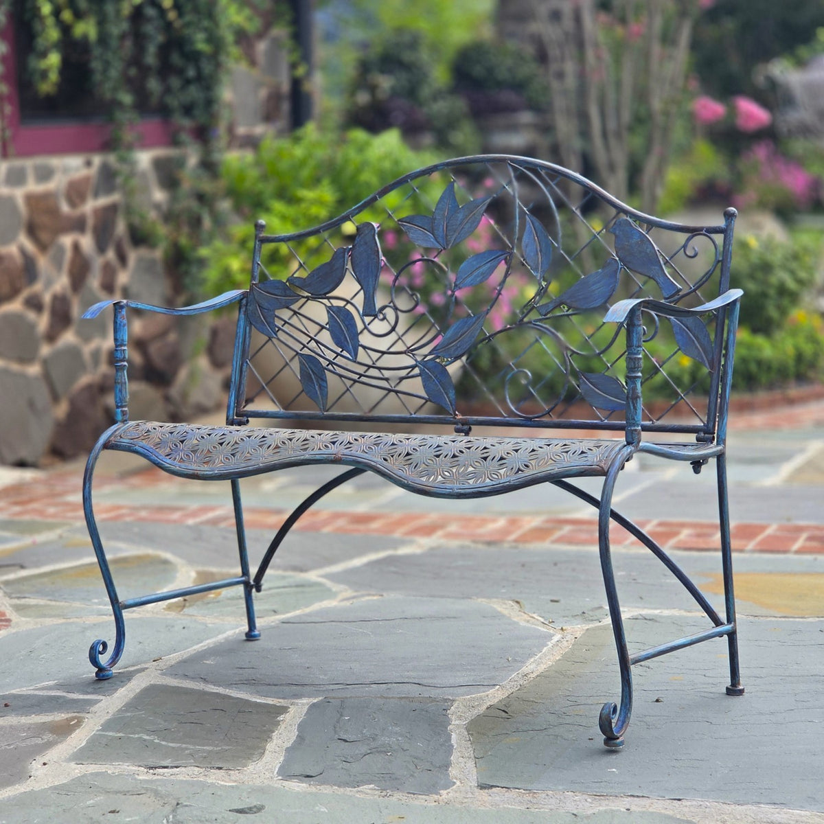 Ornate dark metal garden bench with bird-and-leaf backrest on a stone patio.