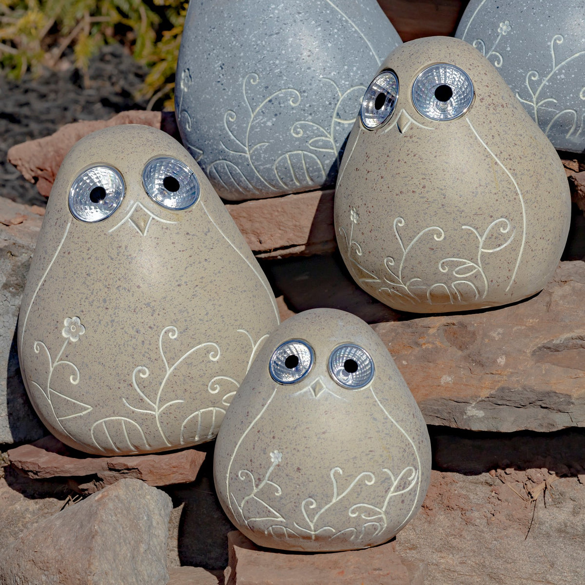 Close view of three beige bird ornaments with floral linework arranged on rocks.