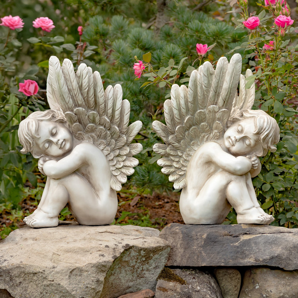 Pair of sitting cherub statues displayed on a stone ledge among flowers