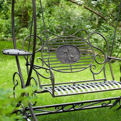 The slatted swing seat and floral backrest sit between curled metal supports, with a small side tray visible.