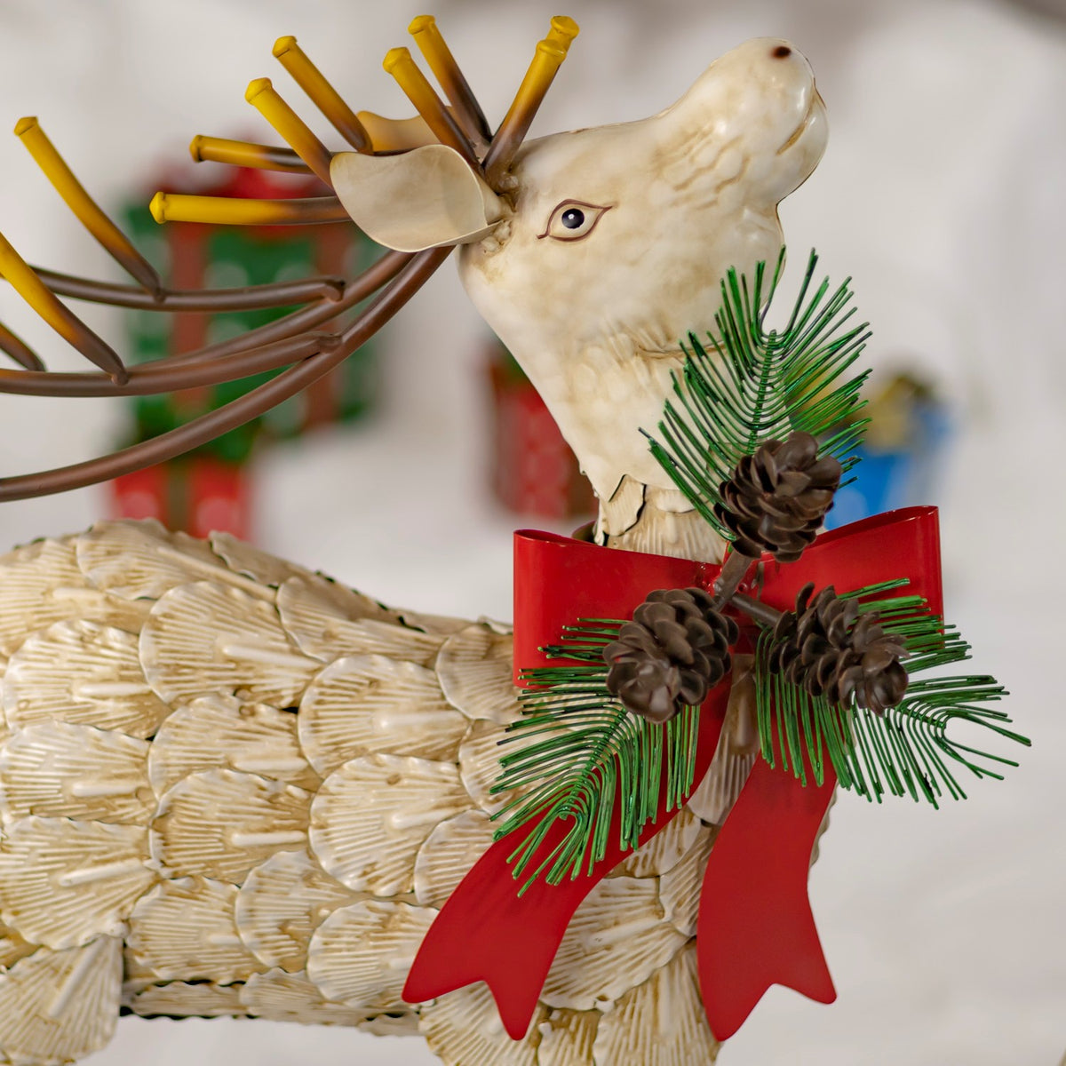 Close-up of a cream reindeer head and red bow with pinecone greenery