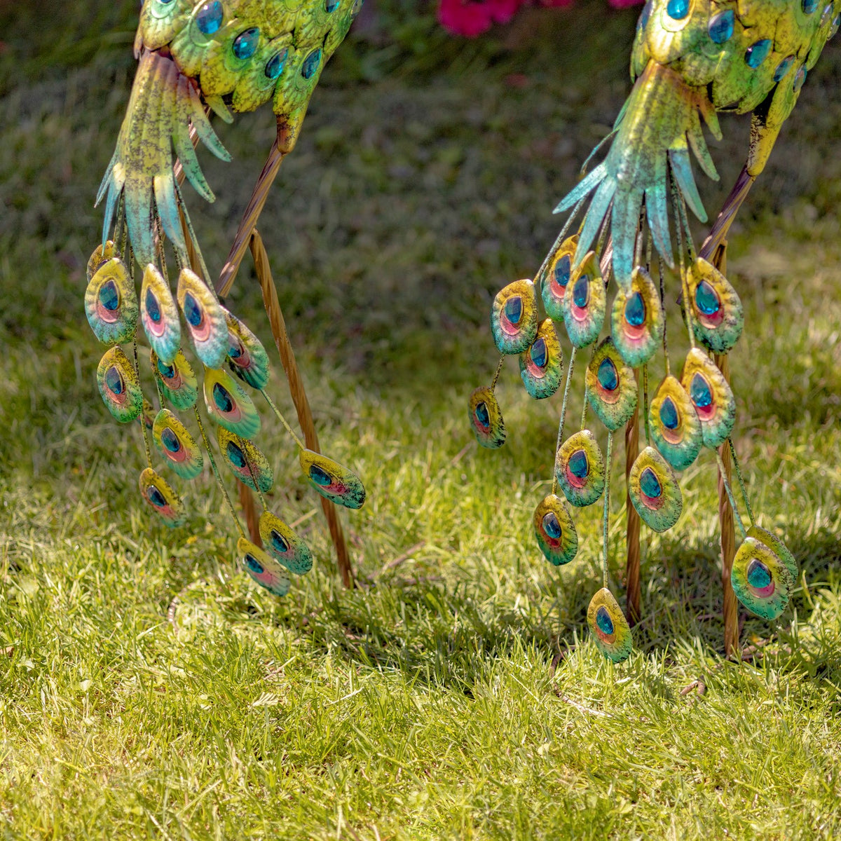 Detail of jeweled metal tail feathers from two peacock statues on grass