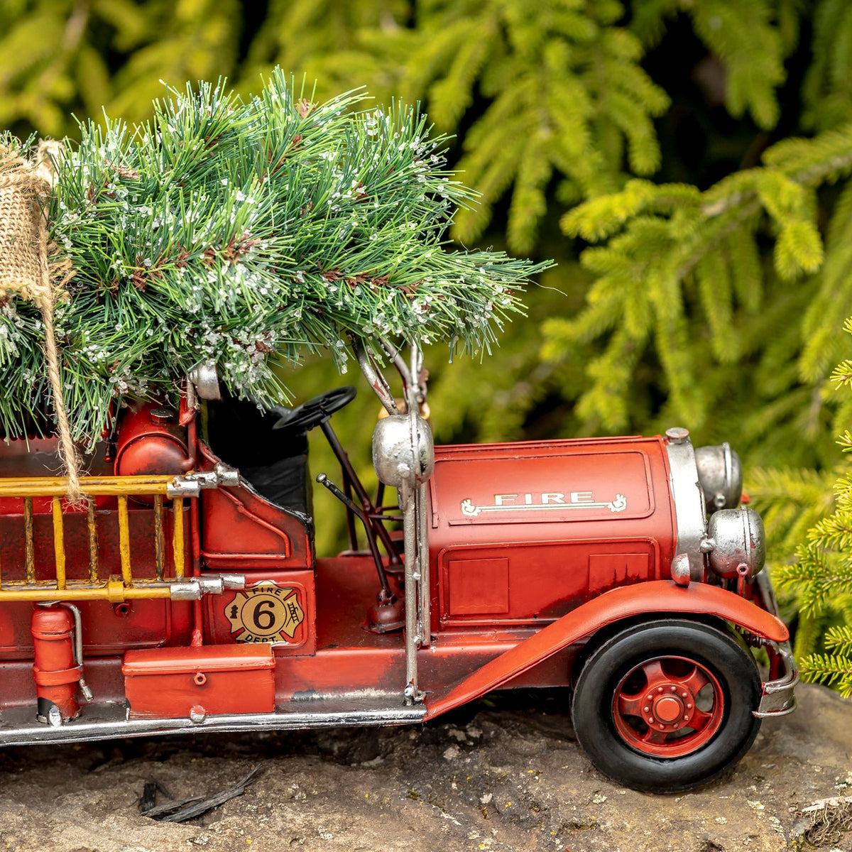 Red vintage-style fire truck carrying a snow-dusted evergreen tree, shown from the side.